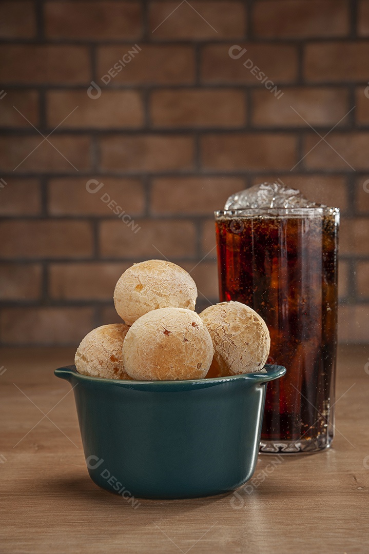 Pães de queijo em um ramekin verde com um copo de refrigerante de cola na mesa de madeira e fundo de parede de tijolos.