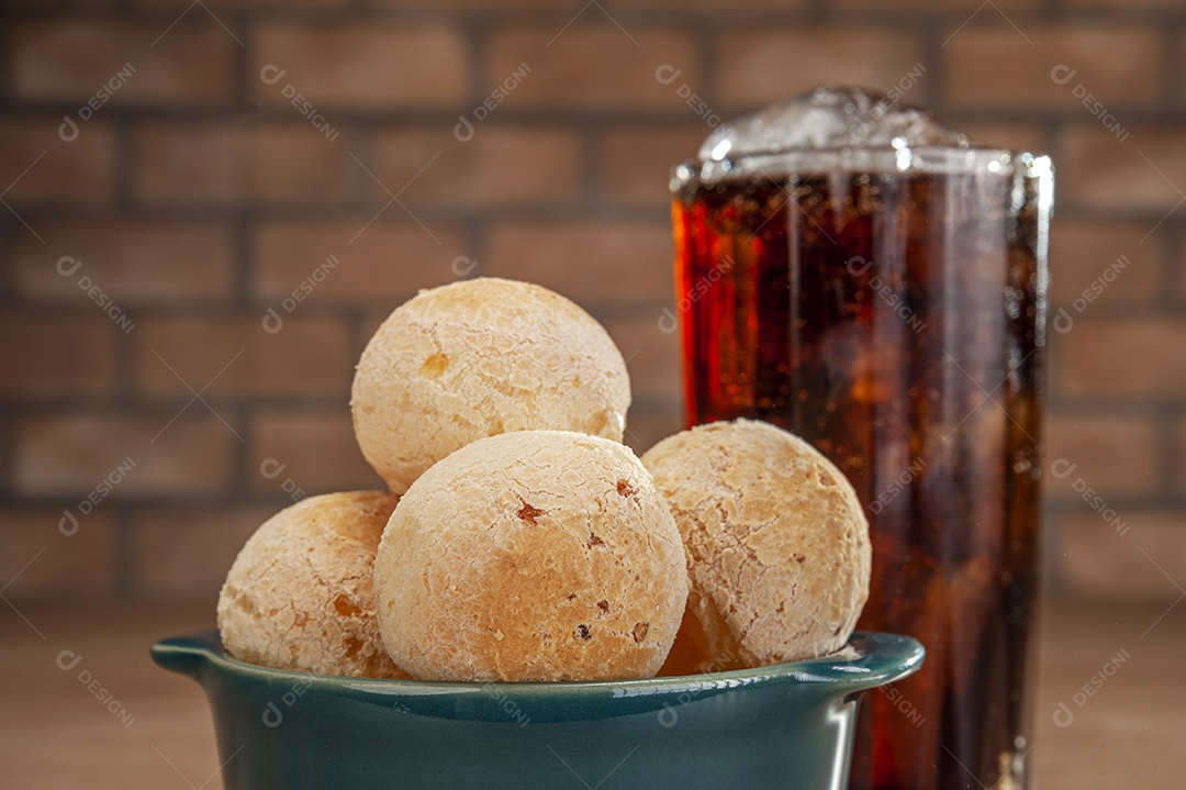 Pães de queijo em um ramekin verde com um copo de refrigerante de cola na mesa de madeira e fundo de parede de tijolos.