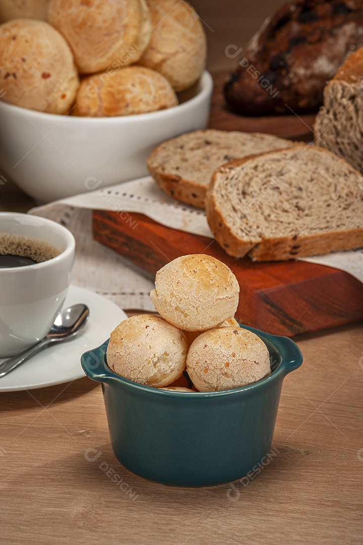 Pães de queijo em um ramekin verde com uma xícara de café na mesa de madeira e fundo de parede de tijolos.