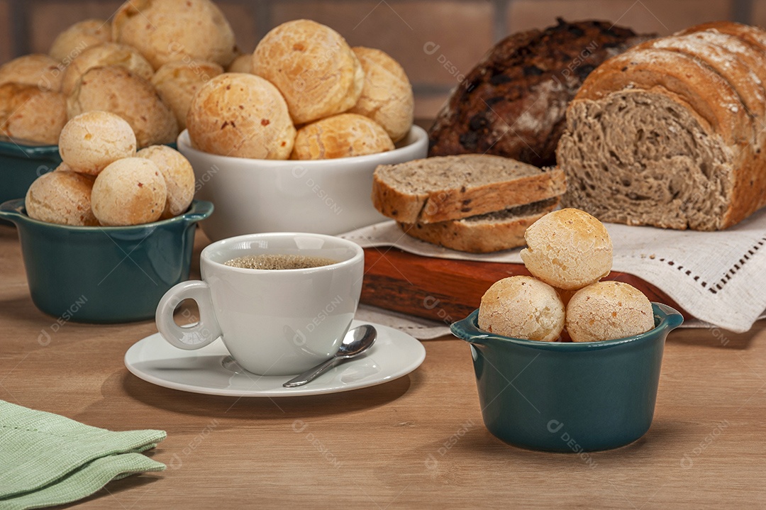 Pães de queijo em um ramekin verde com uma xícara de café na mesa de madeira e fundo de parede de tijolos.