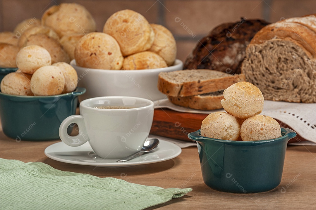 Pães de queijo em um ramekin verde com uma xícara de café na mesa de madeira e fundo de parede de tijolos.