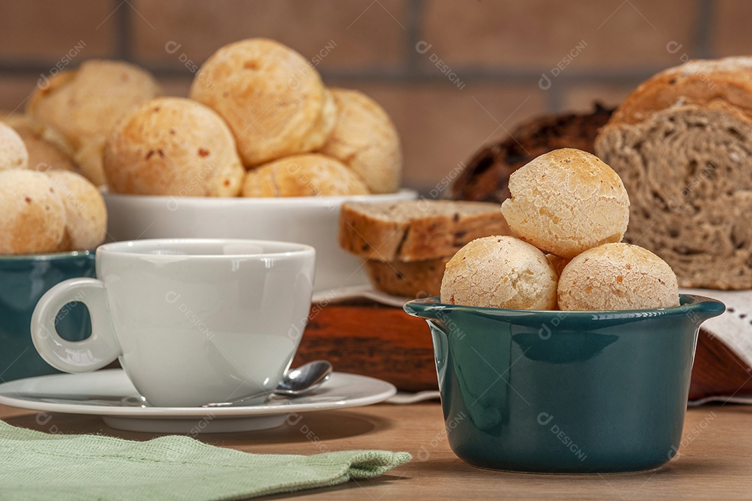 Pães de queijo em um ramekin verde com uma xícara de café na mesa de madeira e fundo de parede de tijolos.