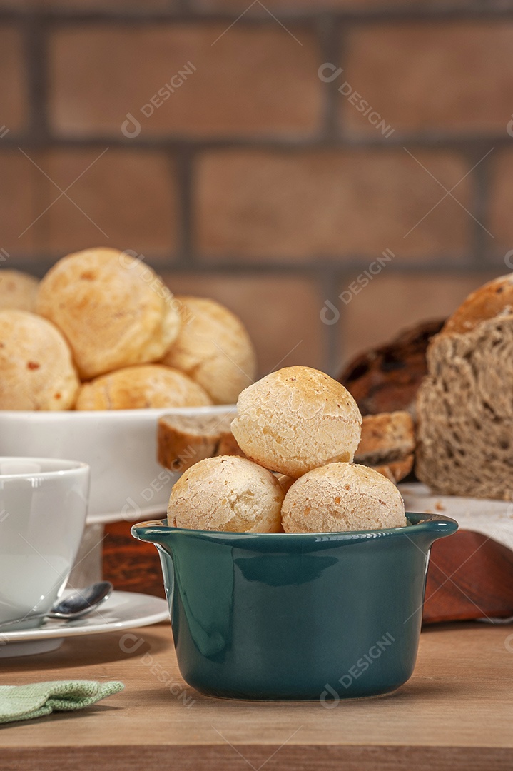 Pães de queijo em um ramekin verde com uma xícara de café na mesa de madeira e fundo de parede de tijolos.