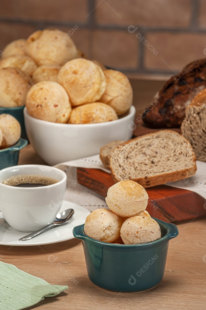 Pães de queijo em um ramekin verde com uma xícara de café na mesa de madeira e fundo de parede de tijolos.