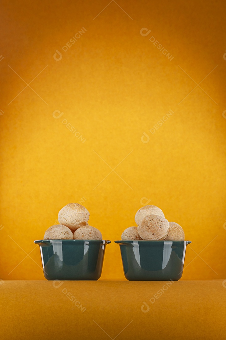 Pães de queijo isolados em dois ramequins verdes sobre fundo laranja.