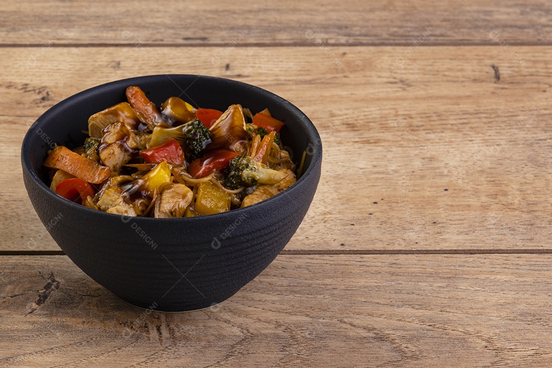 yakissoba de frango em tigela de cerâmica preta na mesa de madeira.