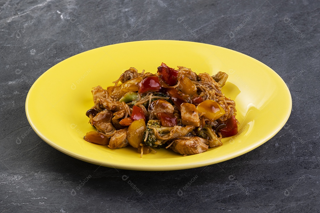 yakisoba com carne de frango em um prato amarelo em uma pedra ardósia escura