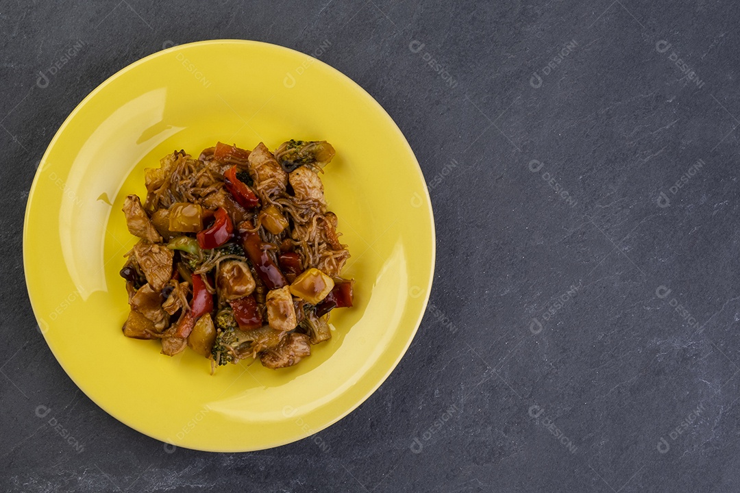 yakisoba com carne de frango em um prato amarelo em uma pedra ardósia escura - vista superior