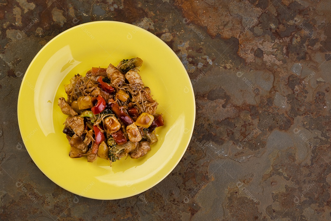 Yakisoba com carne de frango em um prato amarelo em uma pedra de ardósia enferrujada - vista superior