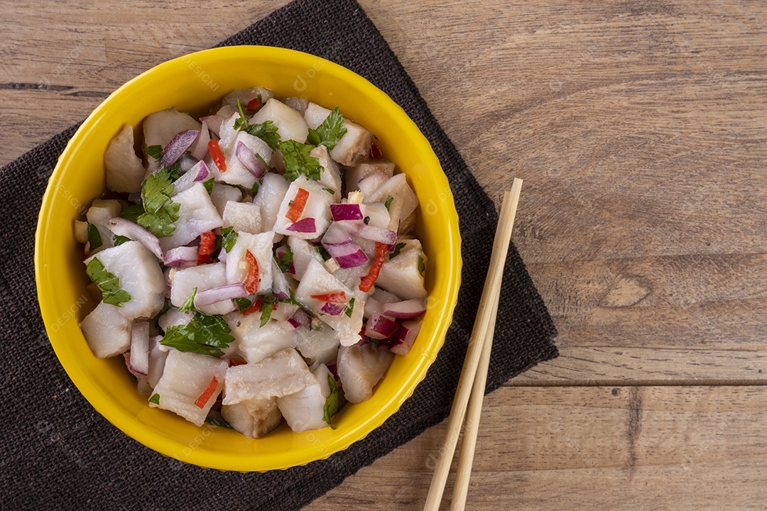 Uma tigela amarela com ceviche em uma mesa de madeira