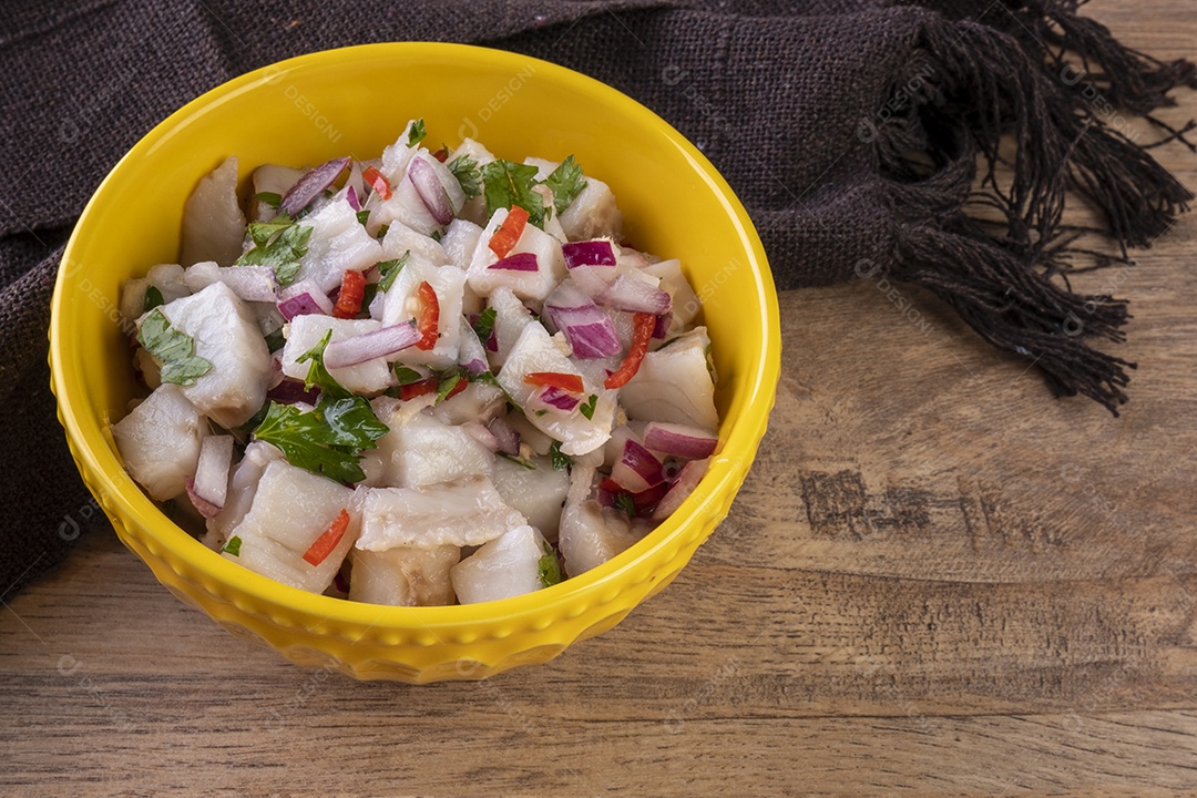 Uma tigela amarela com ceviche em uma mesa de madeira