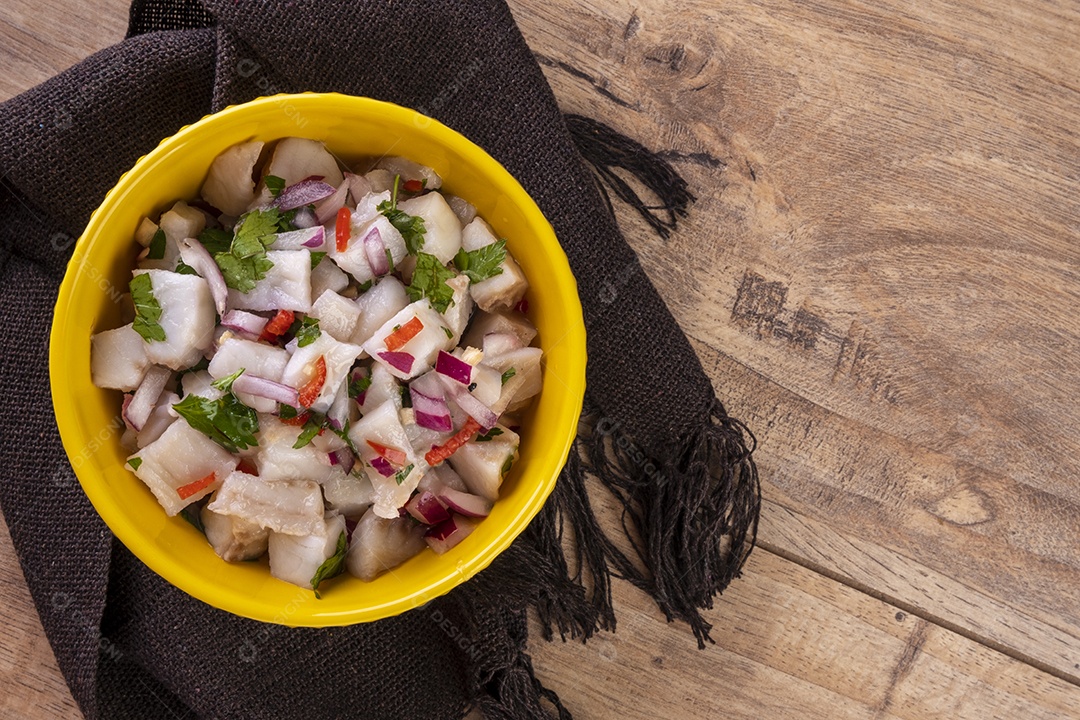 Uma tigela amarela com ceviche em uma mesa de madeira