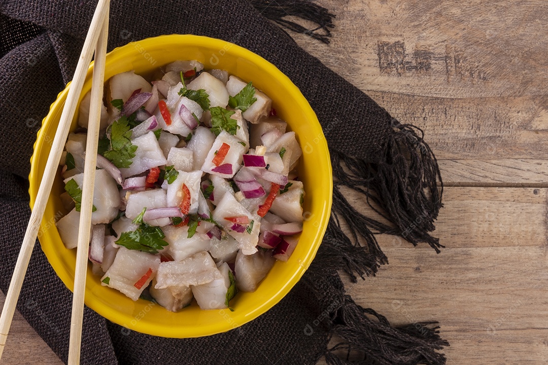 Uma tigela amarela com ceviche em uma mesa de madeira