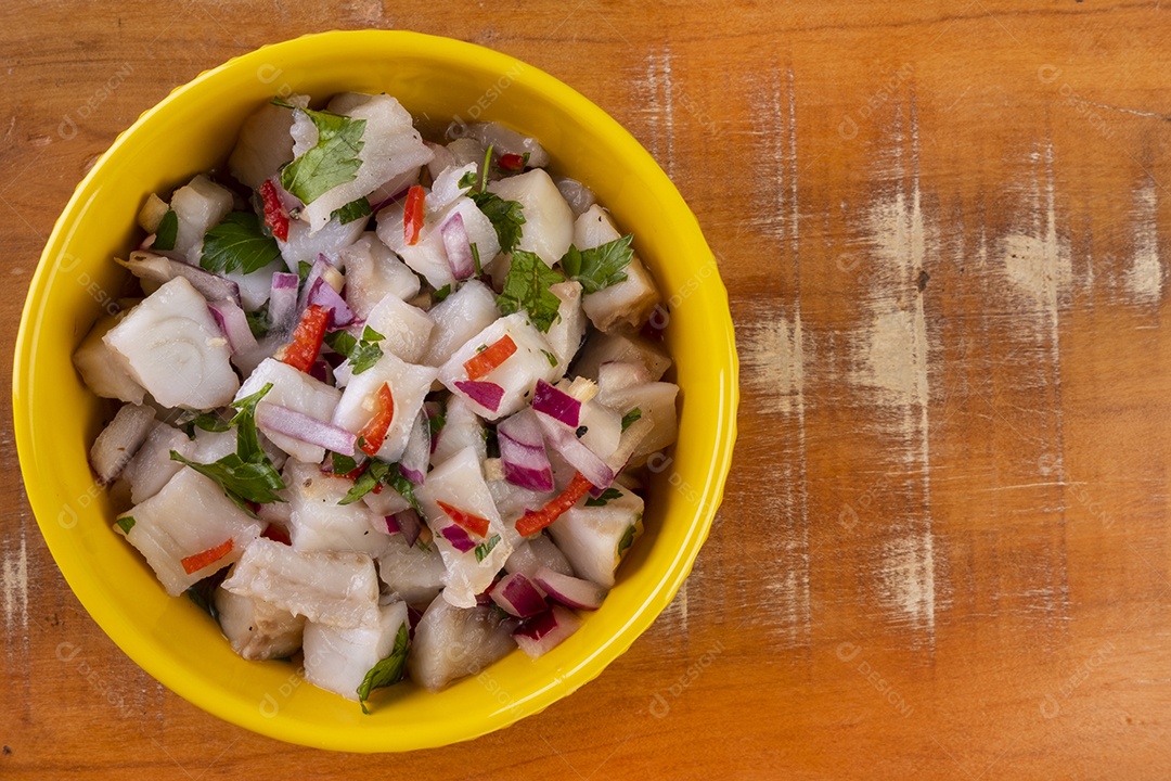 Uma tigela amarela com ceviche em uma mesa de madeira