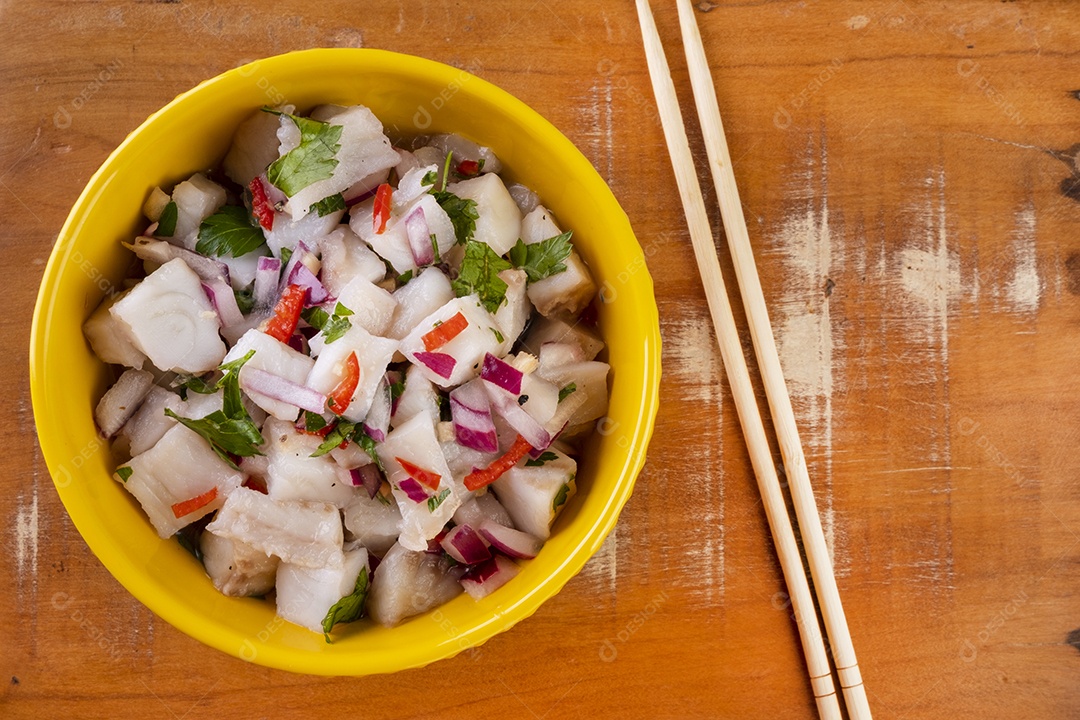 Uma tigela amarela com ceviche em uma mesa de madeira