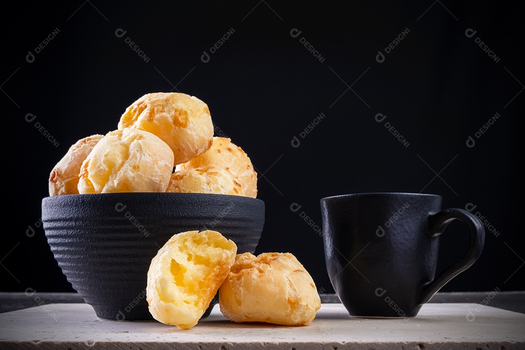 Deliciosos pães de queijo e uma xícara de café em mármore branco com fundo preto.