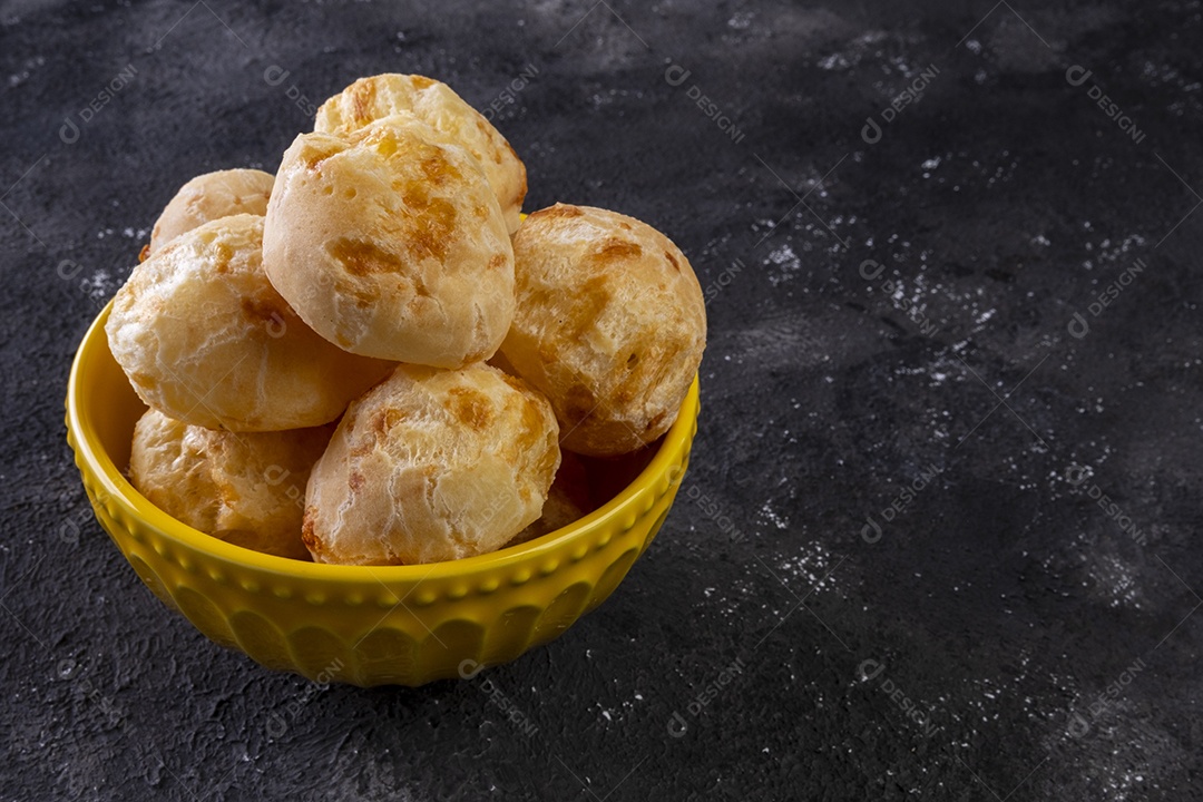 Tigela amarela com pães de queijo em fundo escuro