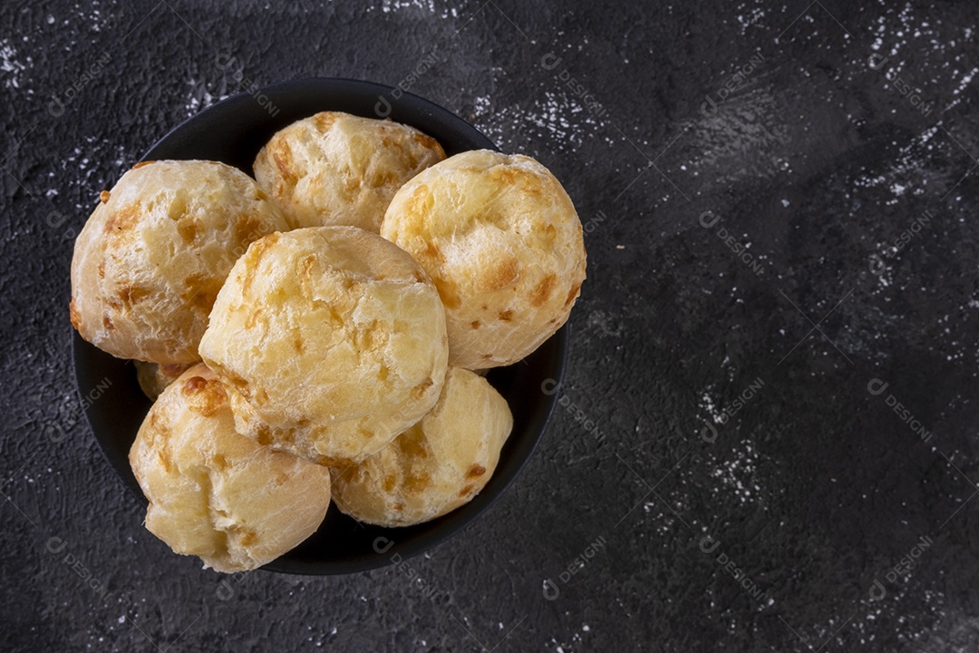 Tigela preta com pães de queijo em fundo escuro
