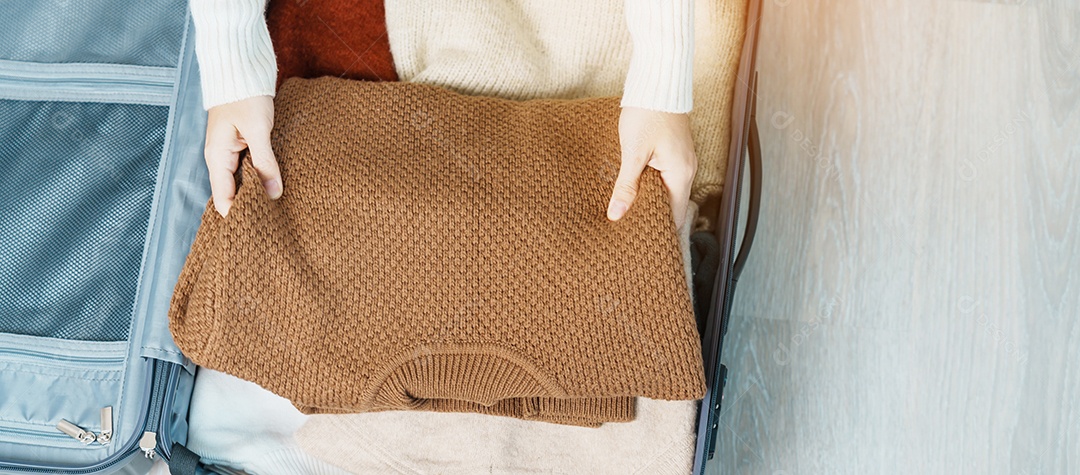 Mão de mulher embalando suas roupas de inverno na bagagem. hora de viajar
