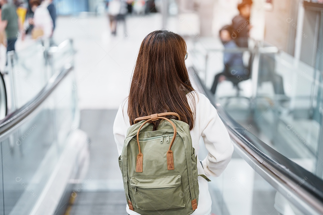 Viajante de mulher asiática com mochila andando na escada rolante no aeroporto internacional.