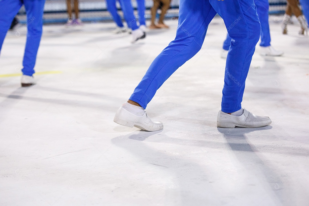 Pernas de um sambista dançando, com calça amarela e sapatos brancos no Sambódromo da Marques de Sapucai, no Rio de Janeiro, Brasil.