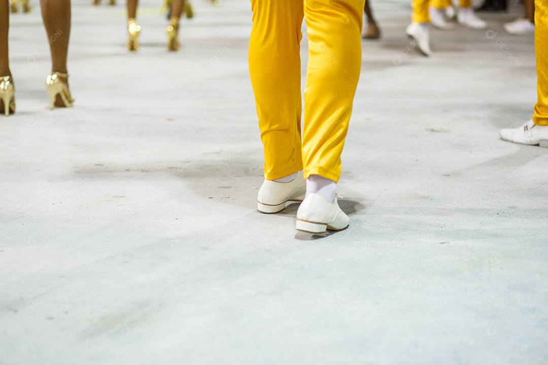Pernas de um sambista dançando, com calça amarela e sapatos brancos no Sambódromo da Marques de Sapucai, no Rio de Janeiro, Brasil.