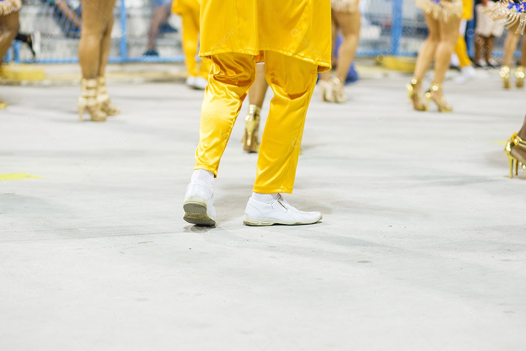Pernas de um sambista dançando, com calça amarela e sapatos brancos no Sambódromo da Marques de Sapucai, no Rio de Janeiro, Brasil.