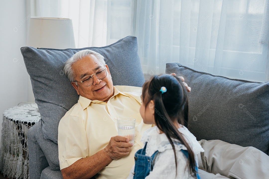 Família feliz A netinha asiática carregava uma droga e um copo dágua para o avô doente no sofá da casa