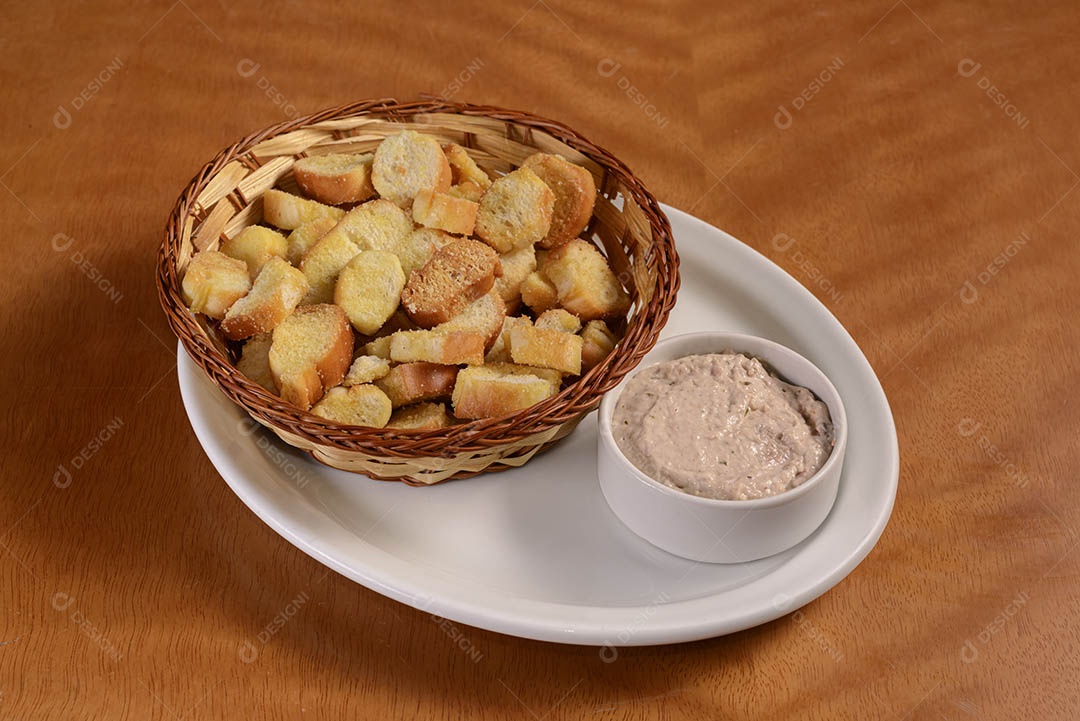 Porção de pão torrado brasileiro com patê na mesa de madeira.