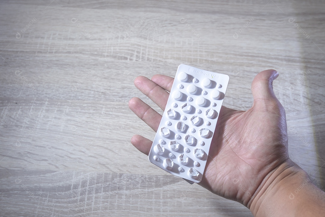 Mão humana segurando pílulas de remédio, luz de fundo de madeira.