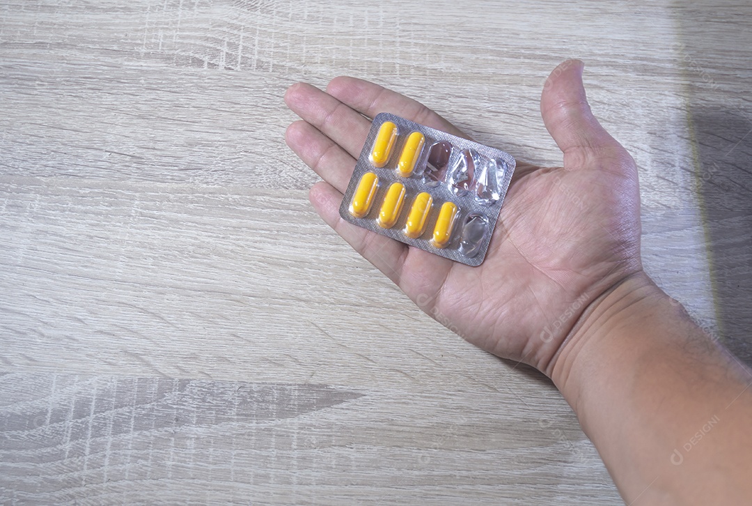 Mão humana segurando pílulas de remédio, luz de fundo de madeira.