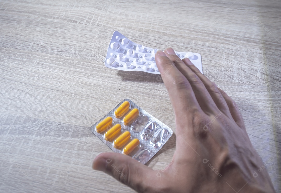 Mão humana segurando pílulas de remédio, luz de fundo de madeira.