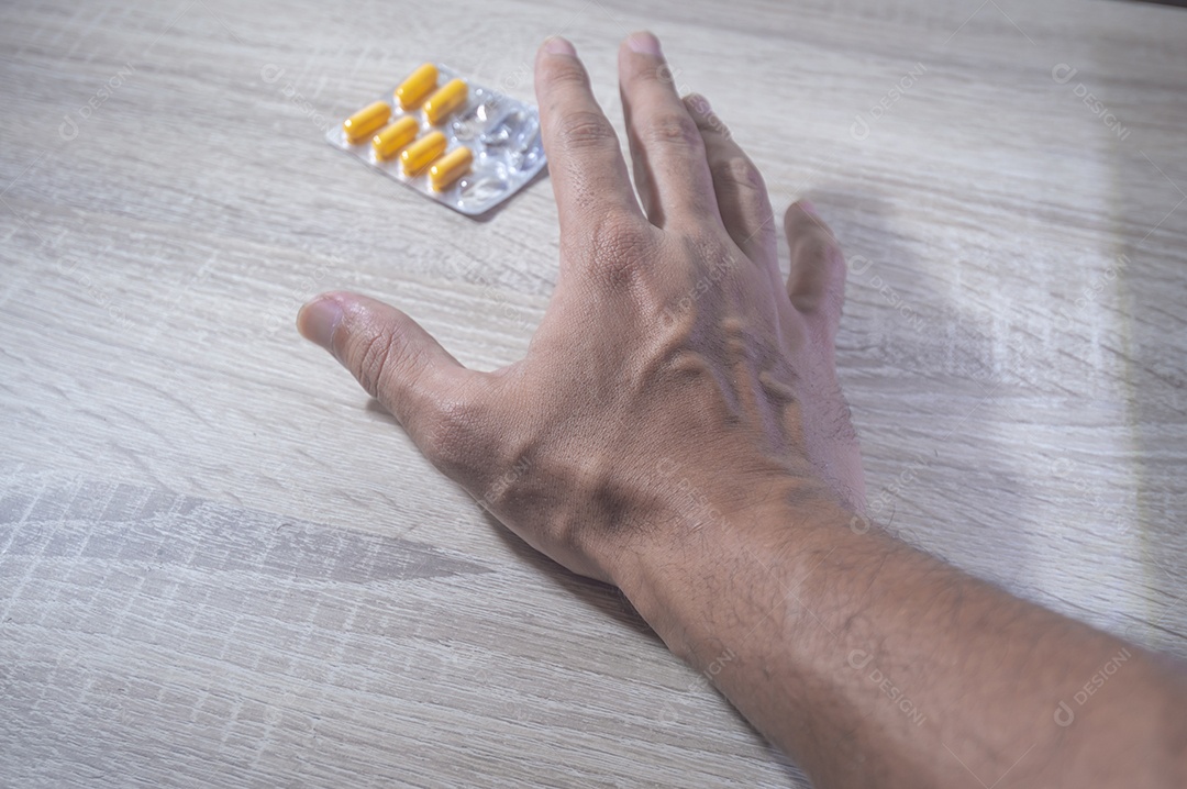 Mão humana segurando pílulas de remédio, luz de fundo de madeira.