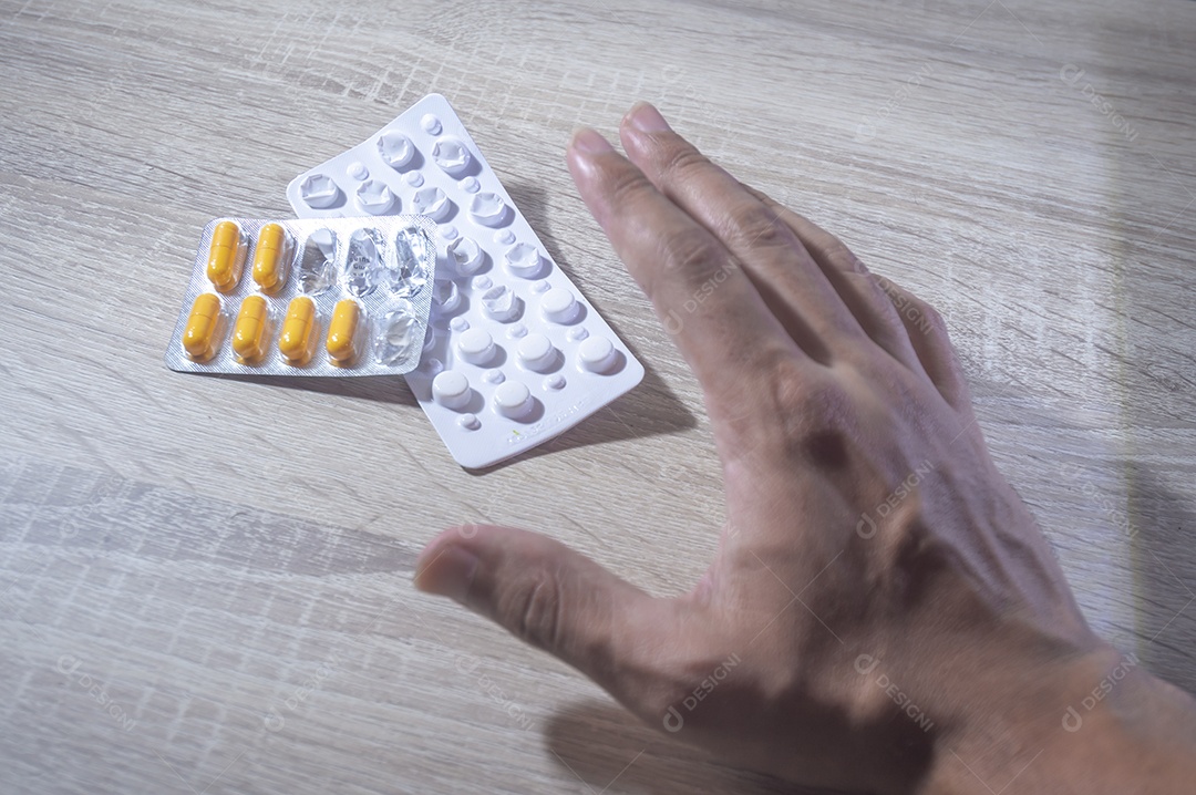 Mão humana segurando pílulas de remédio, luz de fundo de madeira.