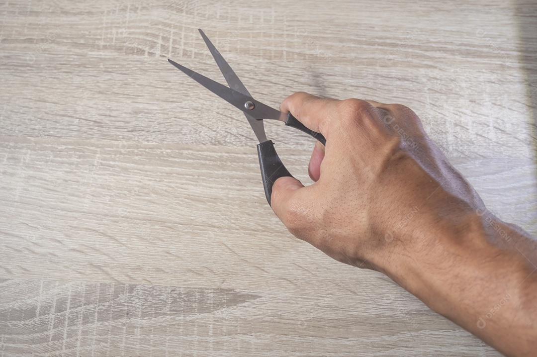 Mão segurando uma tesora, fundo branco de madeira, foto para recorte.