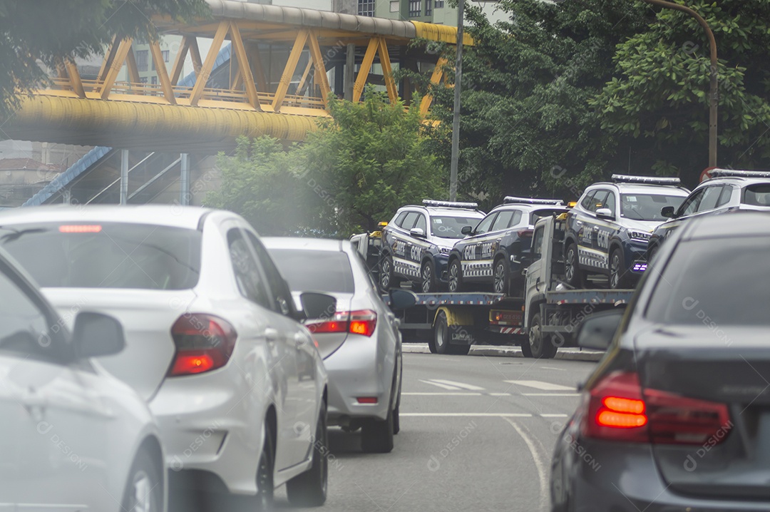 Carros de polícia no trânsito sendo transportados por um guincho.