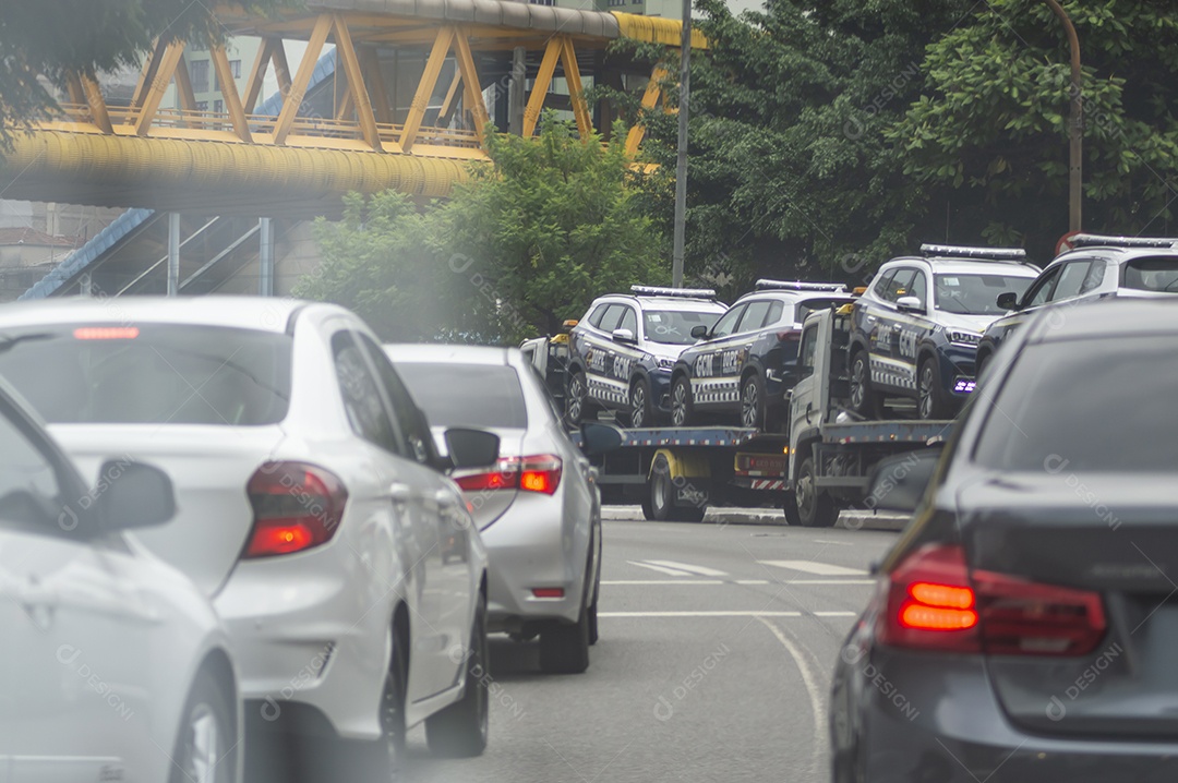 Carros de polícia no trânsito sendo transportados por um guincho.