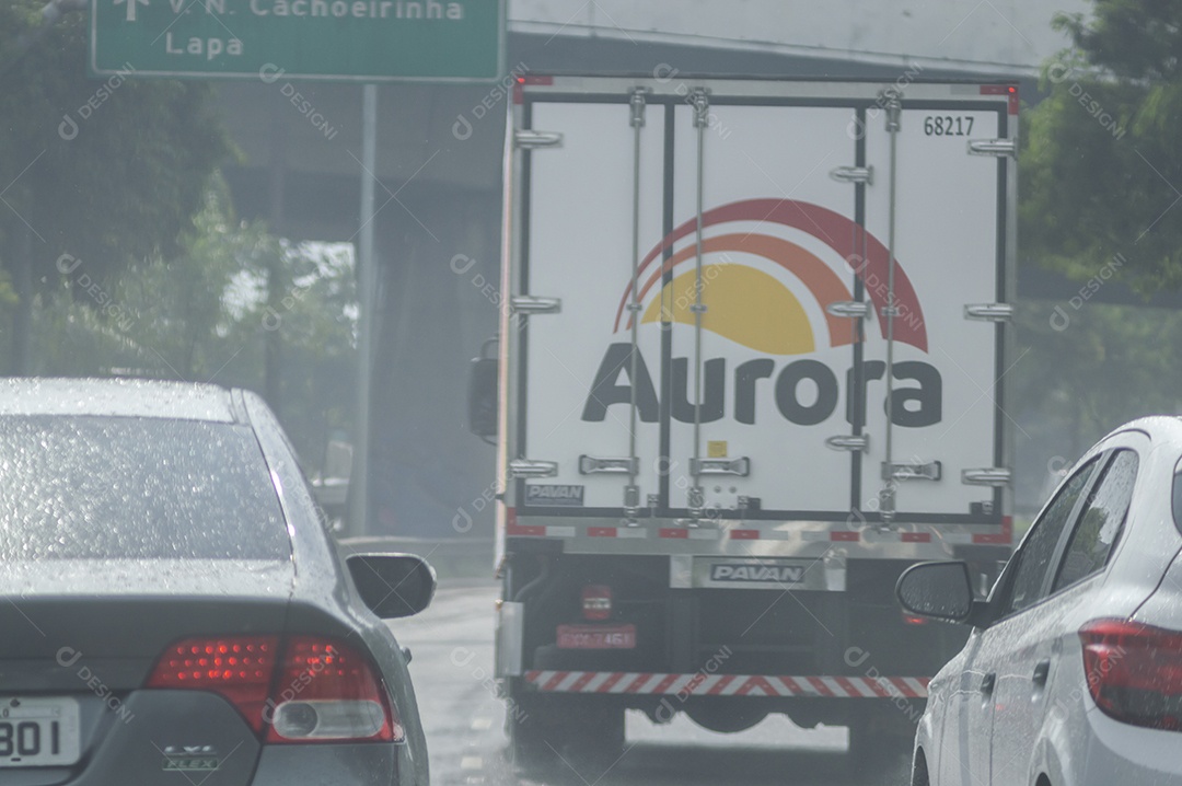 Caminhão da marca brasileira aurora passando por uma avenida em um dia chuvoso.