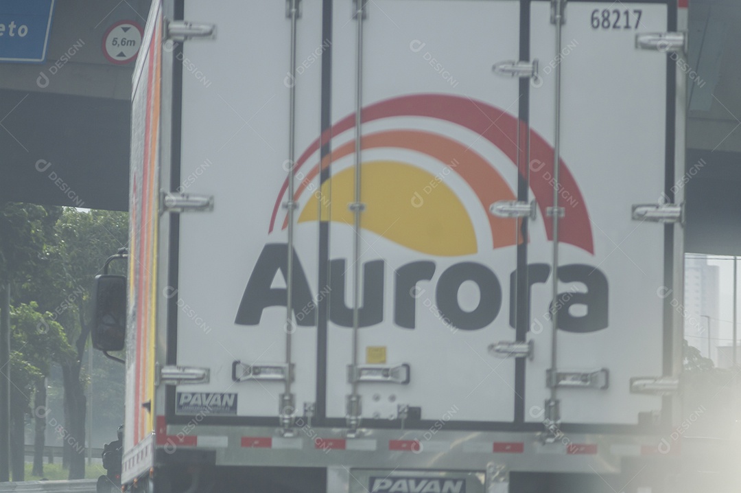 Caminhão da marca brasileira aurora passando por uma avenida em um dia chuvoso.