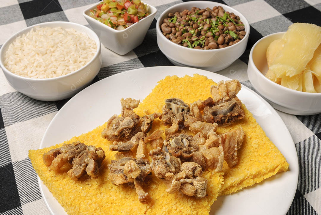 Rabo de boi com cuscuz brasileiro, acompanhado de arroz, feijão, mandioca e vinagrete, em prato branco sobre toalha xadrez preto e branco. Culinária nordestina brasileira.