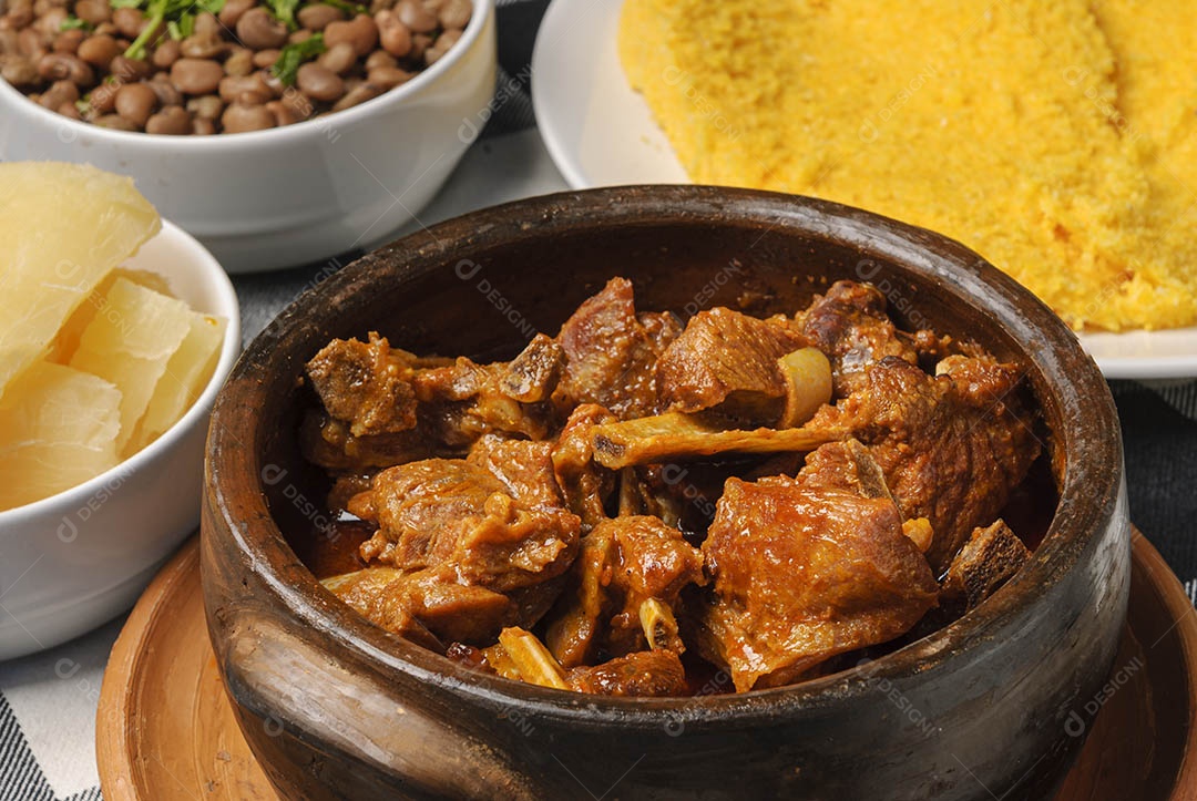 Cabrito assado com cuscuz brasileiro, acompanhado de arroz, feijão, mandioca e vinagrete, em prato branco sobre toalha quadriculada preta e branca. Culinária nordestina brasileira.