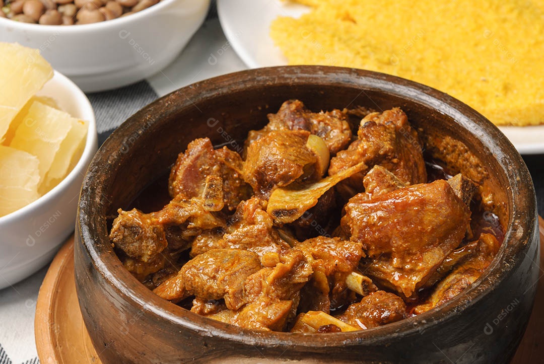 Cabrito assado com cuscuz brasileiro, acompanhado de arroz, feijão, mandioca e vinagrete, em prato branco sobre toalha quadriculada preta e branca. Culinária nordestina brasileira.