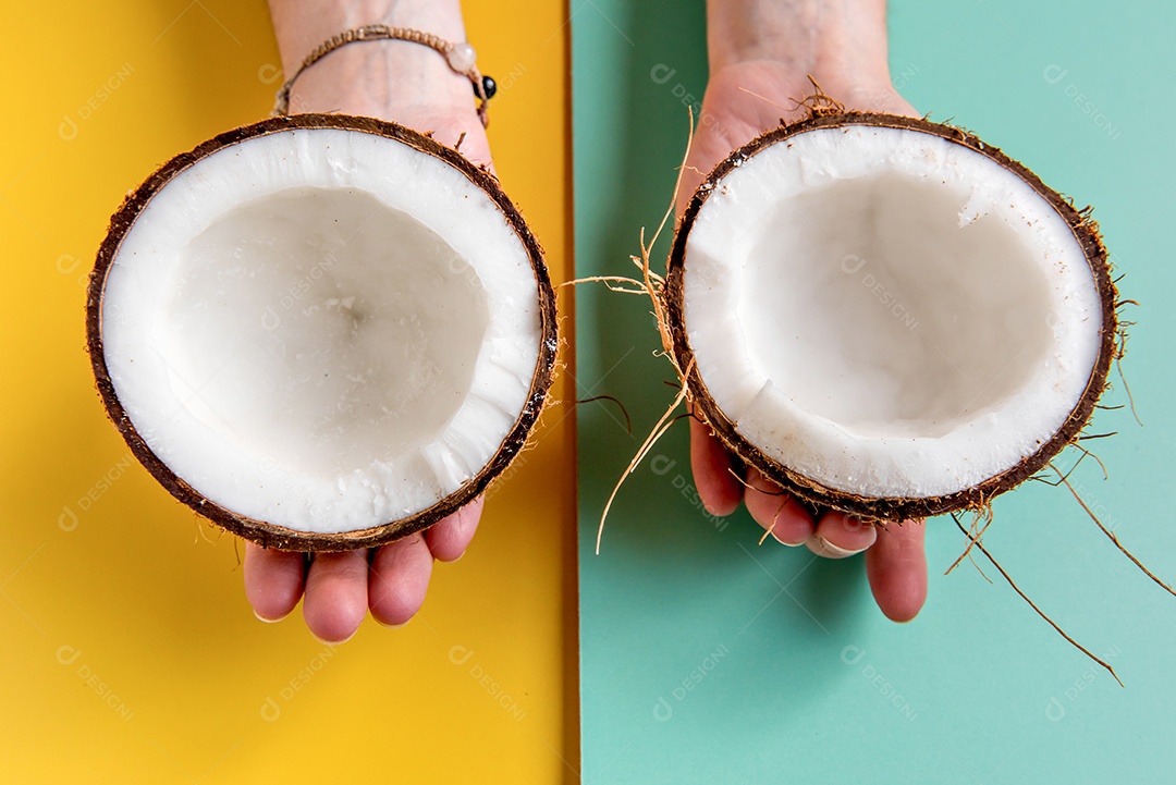 Mãos segurando coco meio cortado em fundo verde e amarelo