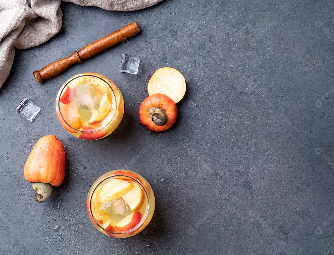 Caipirinha de caju brasileira em copos com gelo e fatias de frutas sobre fundo de pedra