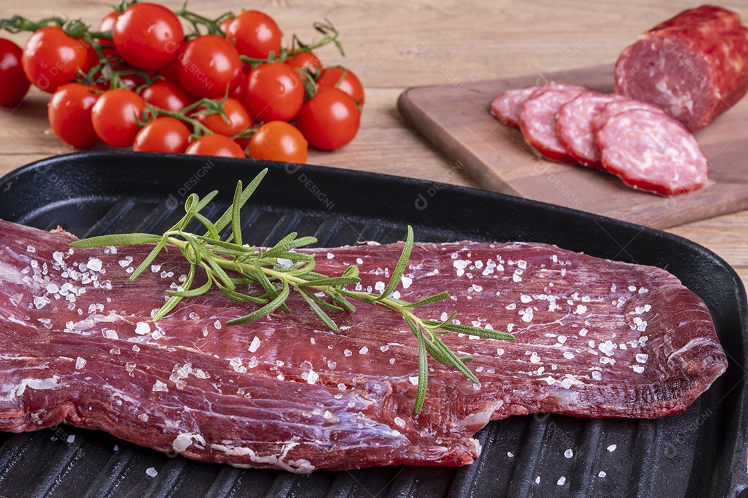 Carne crua salpicada com sal grosso e raminho de alecrim em uma placa de ferro fundido.