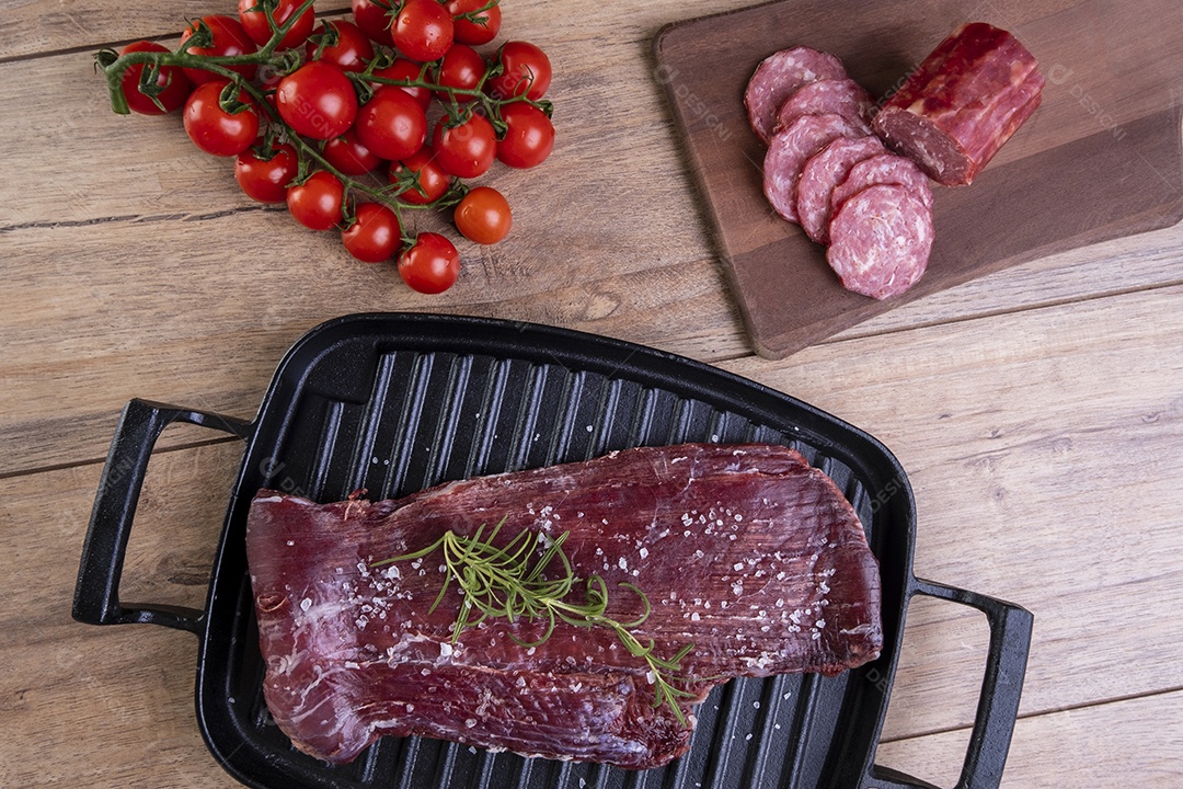 Carne crua salpicada com sal grosso e raminho de alecrim em uma placa de ferro fundido.