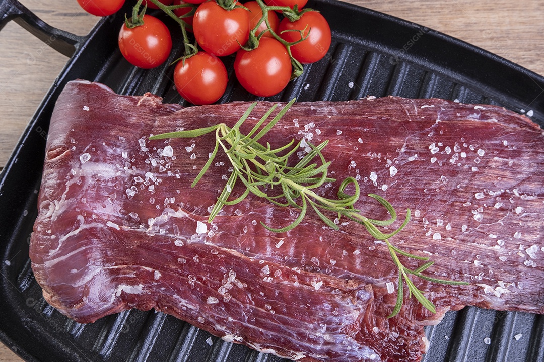 Carne crua salpicada com sal grosso e raminho de alecrim em uma placa de ferro fundido.