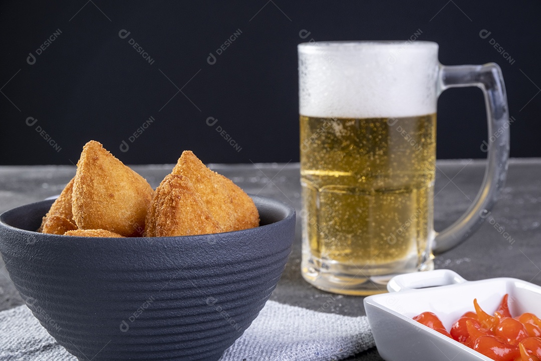 Tradicional petisco brasileiro frito recheado com frango e um copo de cerveja.