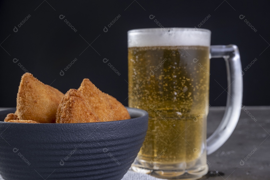 Tradicional petisco brasileiro frito recheado com frango e um copo de cerveja.