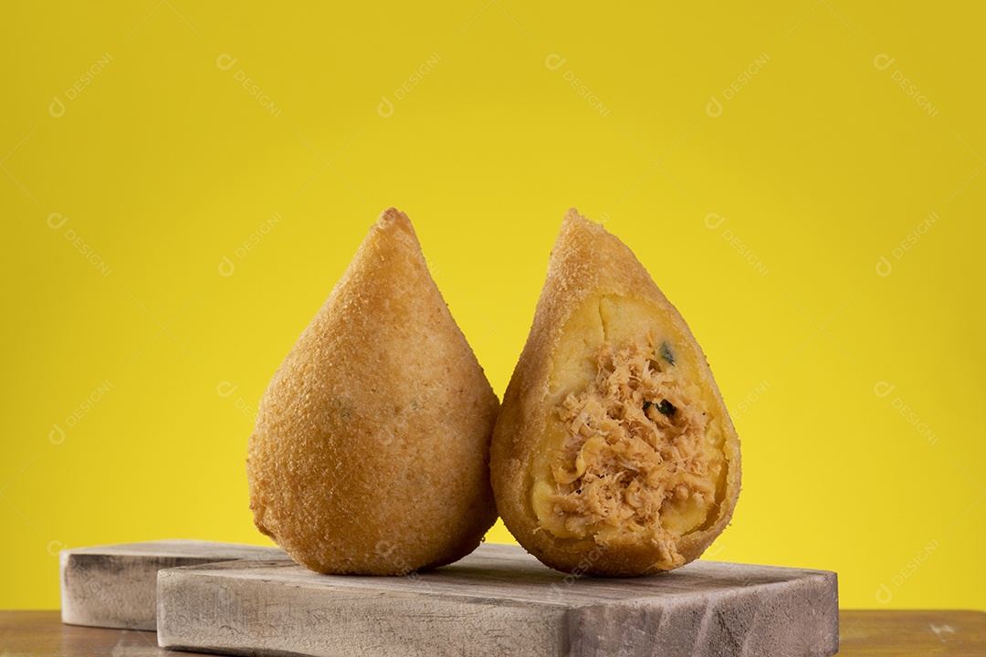 Coxinha frita na tábua de madeira com fundo amarelo